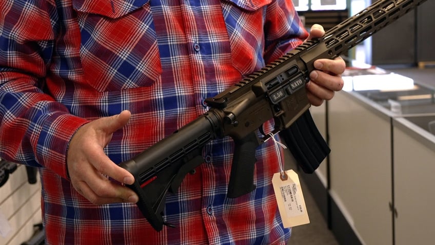 Bryan Zielinski holds semi-automatic rifle with sales tag dangling from trigger guard