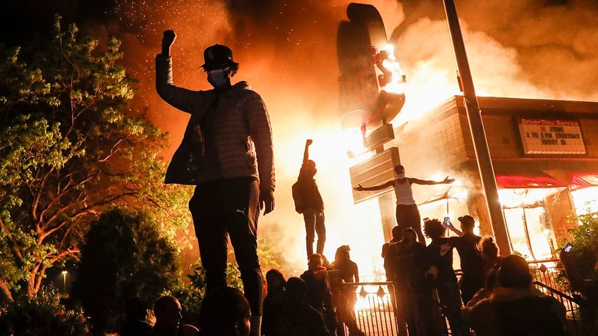 Protestors demonstrate outside of a burning fast food restaurant, Friday, May 29, 2020, in Minneapolis.