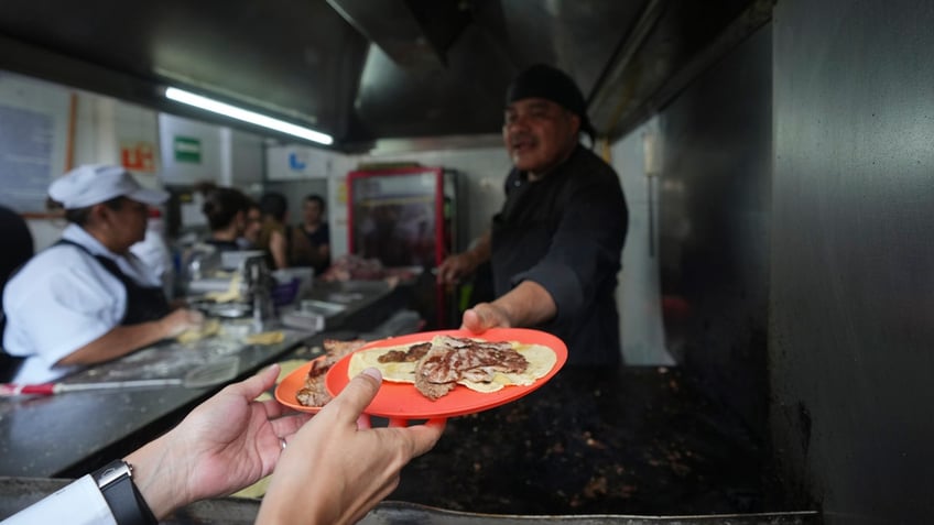 Newly minted Michelin-starred chef Arturo Rivera Martínez hands a customer his order of tacos at the Tacos El Califa de León taco stand, in Mexico City