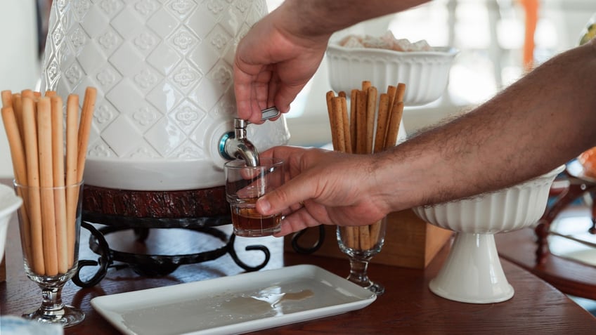 A man pours his own liquor drink from a dispenser on a table.