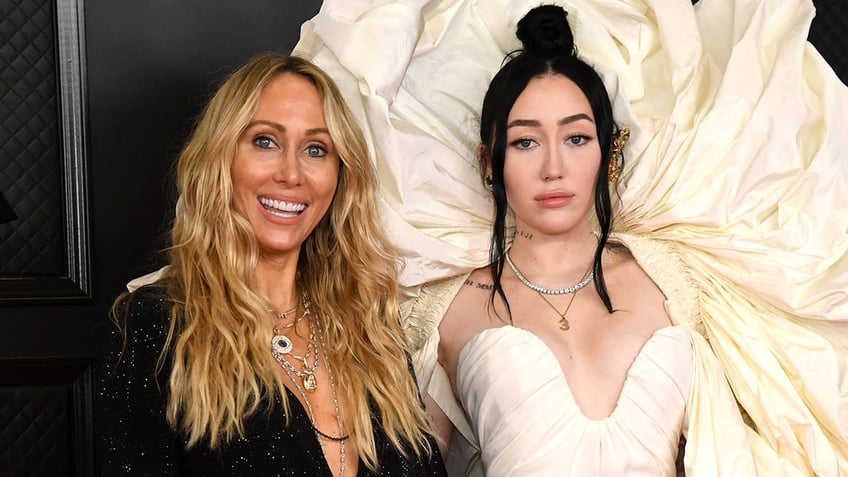 Tish Cyrus in black smiles on the Grammy's carpet with daughter Noah in an off-white dress with a massive shoulder detail