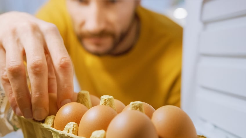 Man reaching into fridge grabbing eggs in foreground