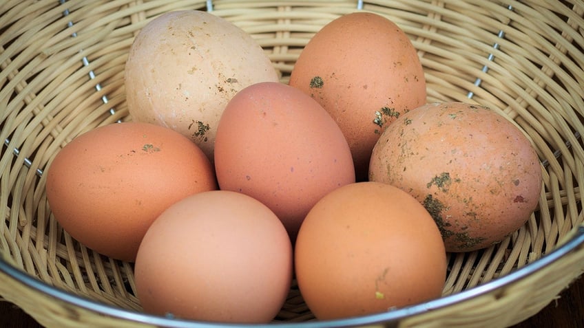 Slightly dirty eggs in a woven basket.