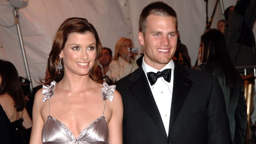 Bridget Moynihan in a silver/metallic dress smiles with Tom Brady in a classic tuxedo at the "Chanel" Costume Institute Gala