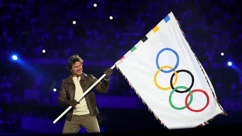 Actor Tom Cruise holds Olympics flag during closing ceremonies.