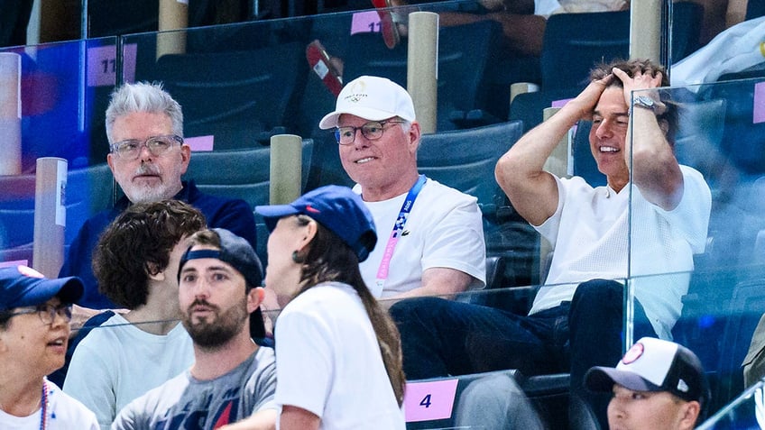 Tom Cruise puts his fingers through his hair and looks stunned while watching the olympics