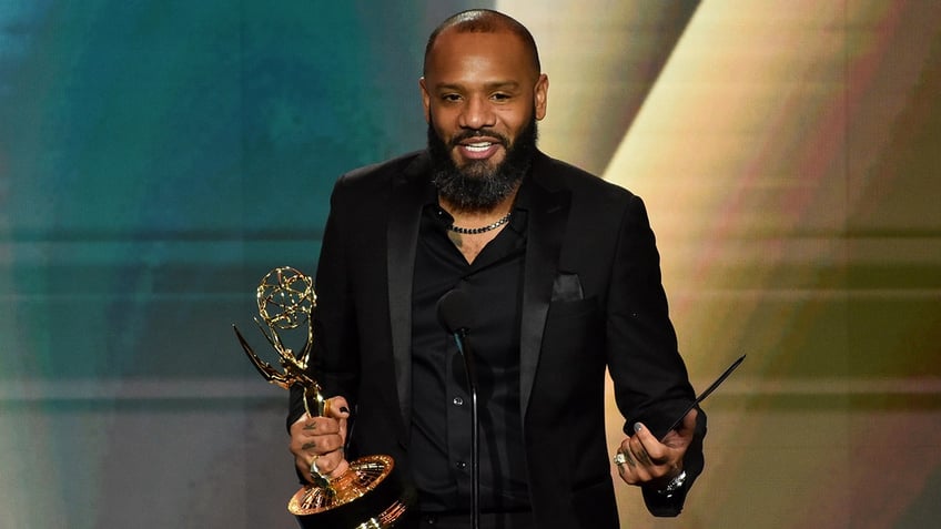 Justin Sutherland in a black suit accepts his Emmy Award on stage