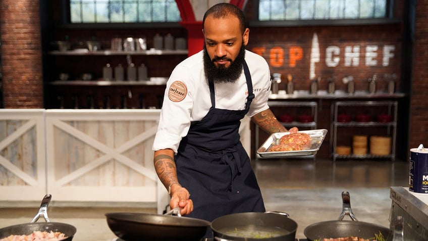 Justin Sutherland holding a pan wearing a black apron