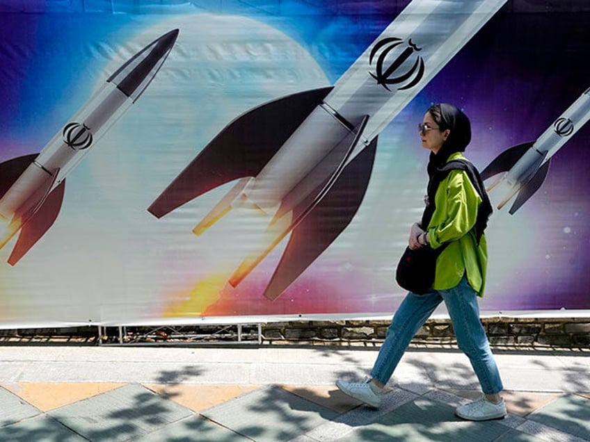 A woman walks past a banner showing missiles being launched, in northern Tehran, Iran, Apr