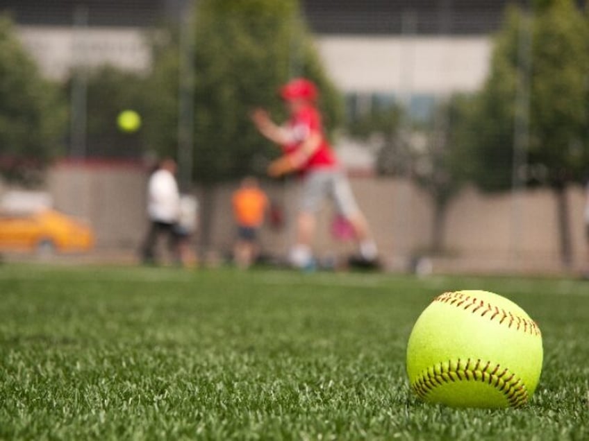 Close-up of softball on the sidelines with girl pitching in the background. turf is artifi