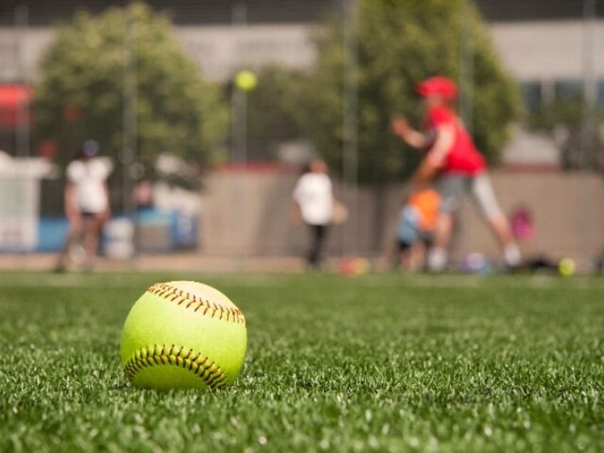Close-up of softball on the sidelines with girl pitching in the background. turf is artifi