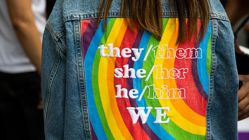 Jacket with pronouns on top of a rainblow flag pattern