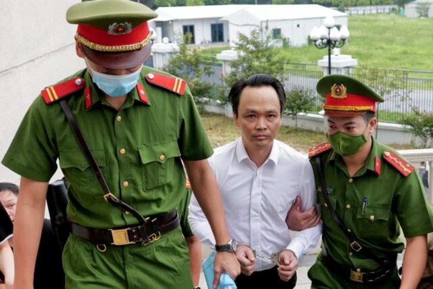 Trinh Van Quyet is escorted by policemen into court at the start of his fraud trial in Han