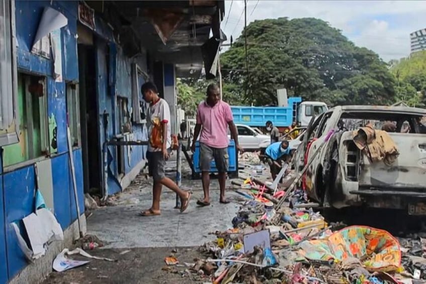 This frame grab from AFPTV video shows people walking past buildings damaged during riots in Port Moresby