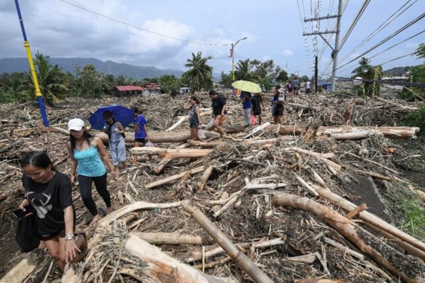 People walk through logs swept away by Tropical Storm Trami in Laurel, Batangas province,