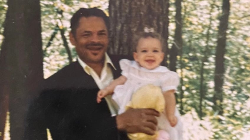 J.C. holding a baby Madison McGhee as he smiles proudly.