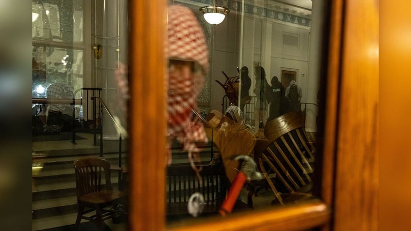 columbia university protestor holds hammer next to door window