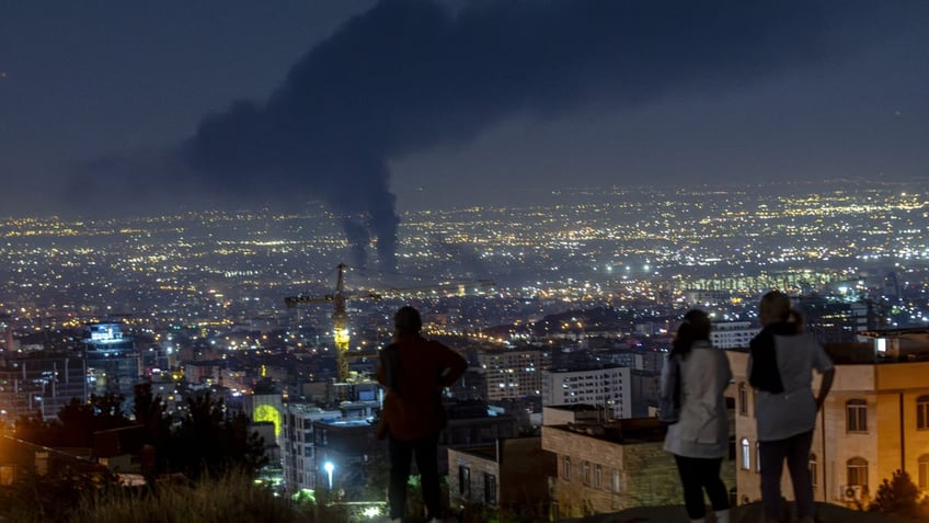 People gather on a hill to watch smoke rising in the distance from an Israeli airstrike in Tehran, Iran, on June 14, 2025. 