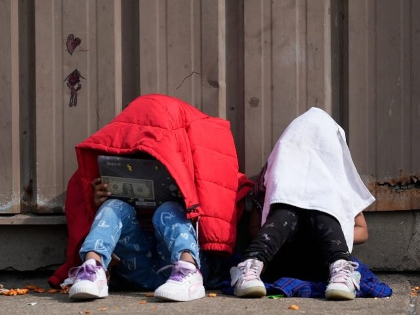 FILE - Children cover their heads as they sit outside of a migrant shelter Wednesday, Marc