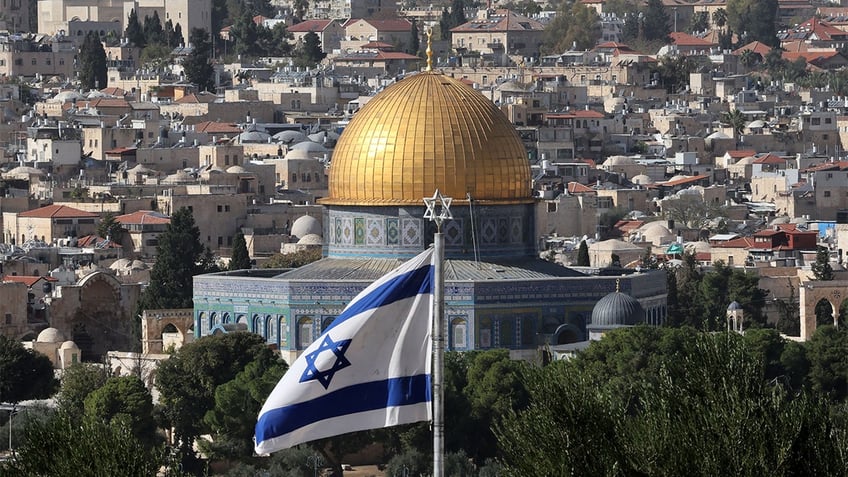 The Israel flag waving in front of the Dome of the Rock.