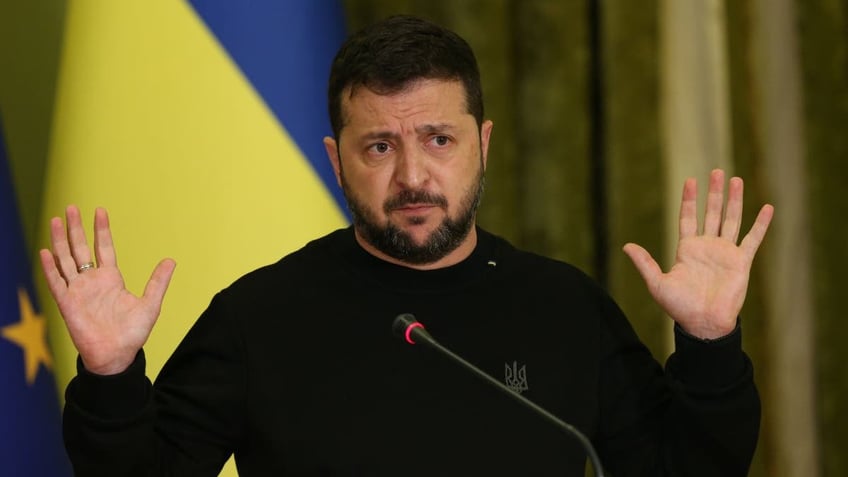 Ukraine President Zelenskyy with Ukraine flag behind him, hands up