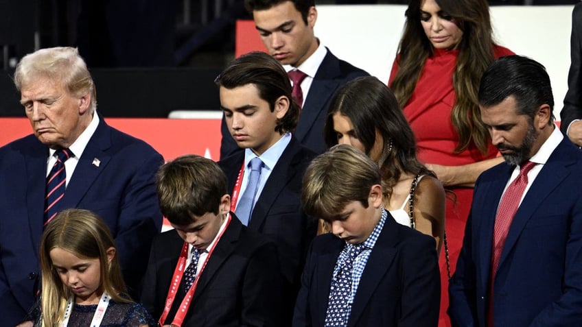 US former President and 2024 Republican presidential candidate Donald Trump bows in prayer alongside his grandchildren during the third day of the 2024 Republican National Convention at the Fiserv Forum in Milwaukee, Wisconsin, on July 17, 2024. Days after he survived an assassination attempt Donald Trump won formal nomination as the Republican presidential candidate and picked Ohio US Senator J.D. Vance for running mate. (Photo by Brendan SMIALOWSKI / AFP) (Photo by BRENDAN SMIALOWSKI/AFP via Getty Images)