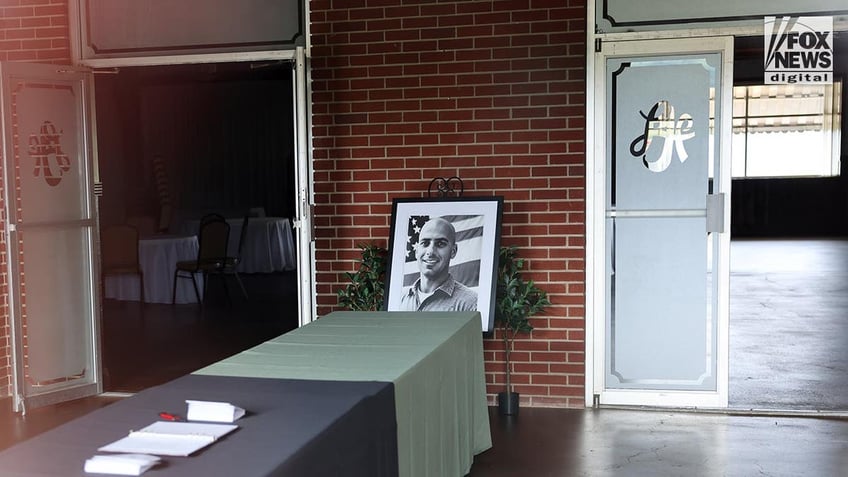 A photo of Comperatore leans against a wall with a visitors' log open on a table