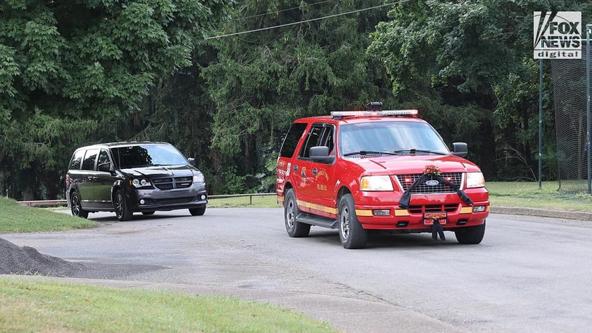 Fire trucks draped in black cloth with a black van following