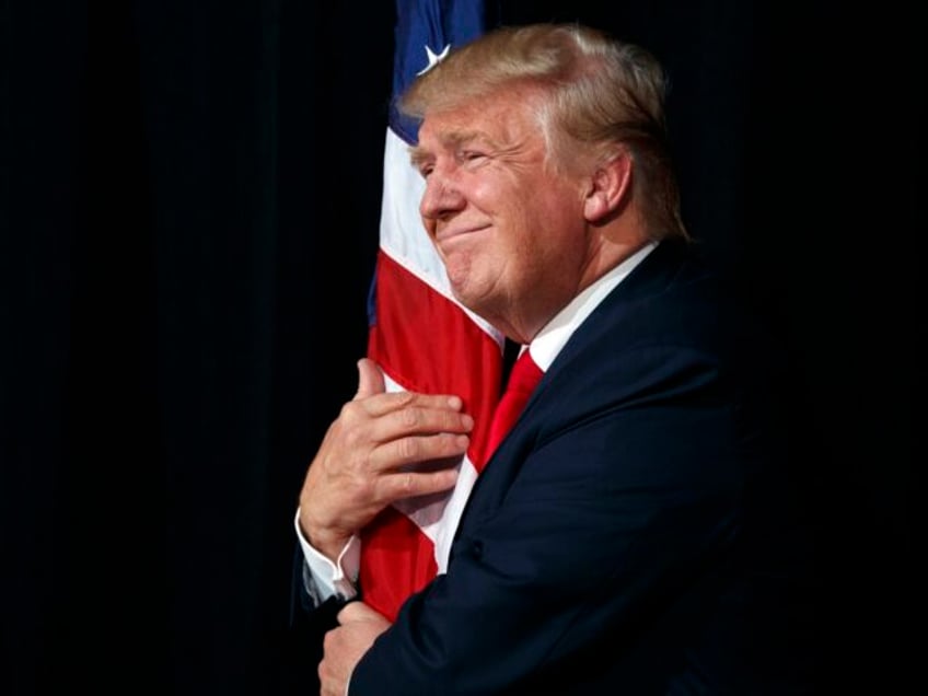 Republican presidential candidate Donald Trump hugs an American flag as he arrives to spea