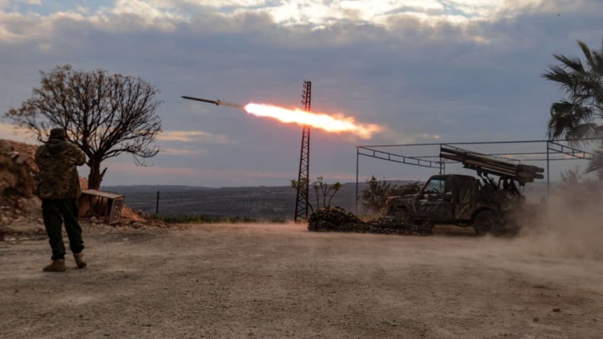 An anti-government fighter covers his ears as a multi-barrel rocket launcher fires against regime forces in the northern outskirts of Syria's west-central city of Hama on December 4, 2024. Syrian government forces pressed a counterattack against Islamist-led rebels around the key city of Hama on December 4 after suffering a string of staggering losses further north, a war monitor said. 