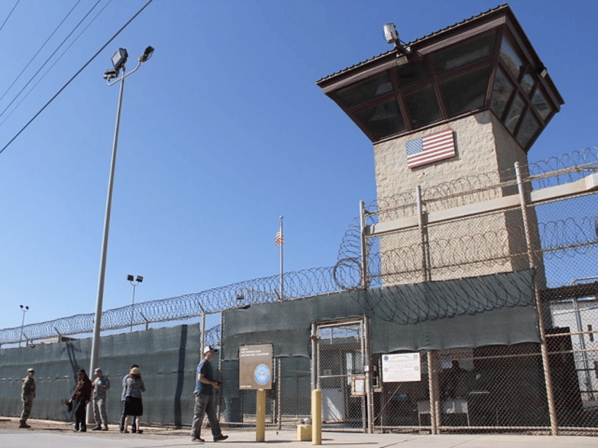 People walk past a guard tower outside the fencing of Camp 5 at the US Military's Prison i