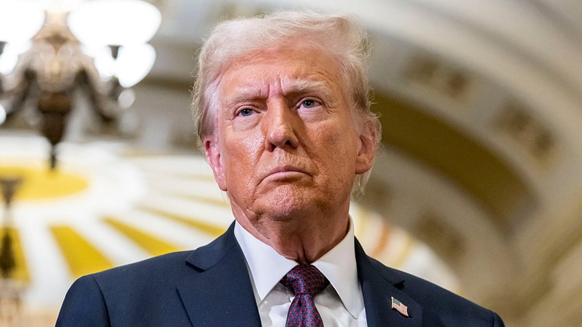 Donald Trump in a navy jacket and purple tie looks to his right