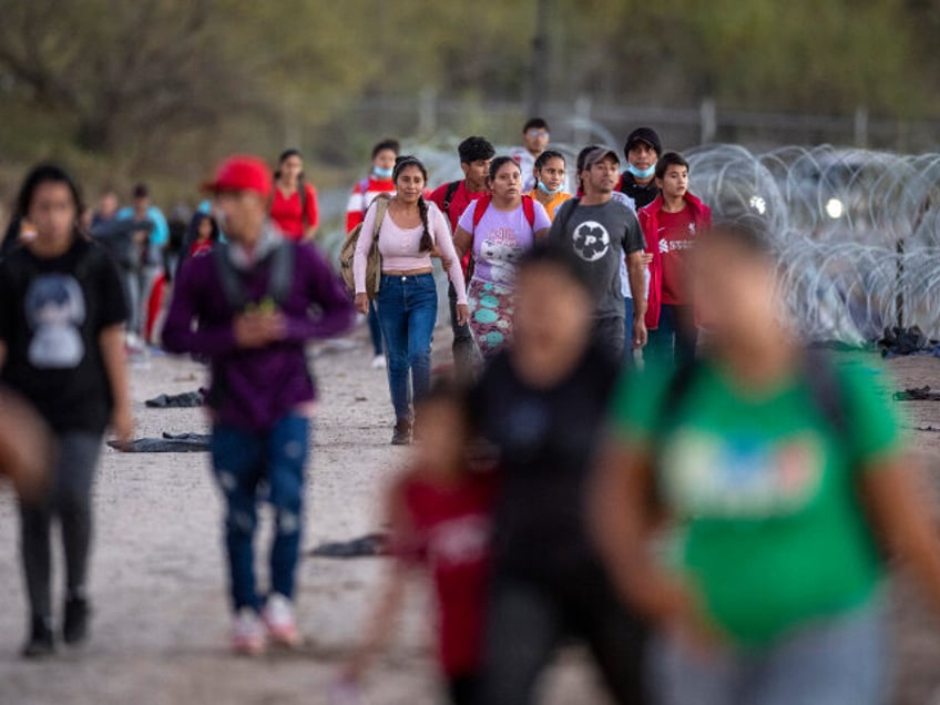 Migrants walk towards a field processing center after crossing from Mexico into the United