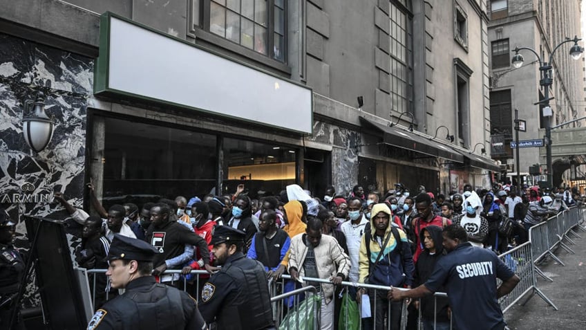 Police officers take security measures as migrants line up outside the Roosevelt Hotel while waiting for placement inside a shelter as asylum seekers camp outside the hotel after the Manhattan relief center is at full capacity in New York City on Aug. 2, 2023. (Photo by Fatih Aktas/Anadolu Agency via Getty Images)