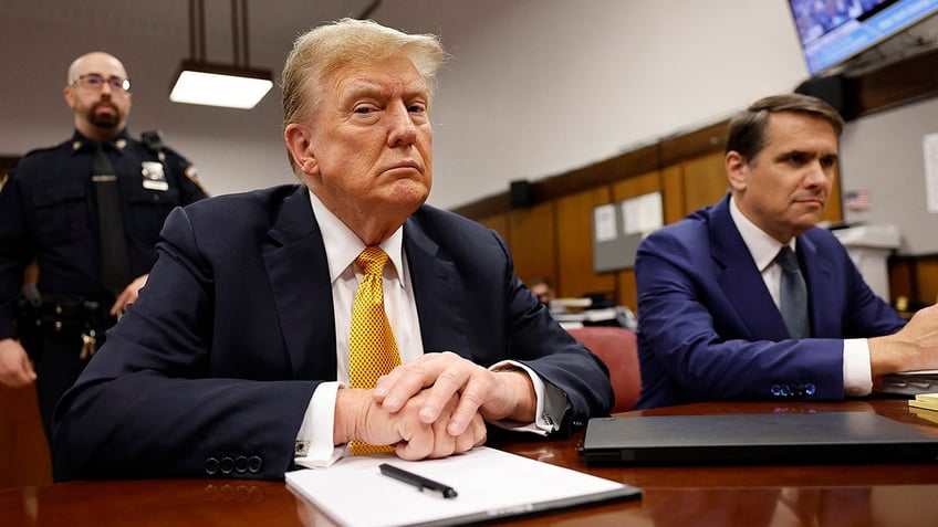 Donald Trump in coat, yellow tie at defense table in courtroom