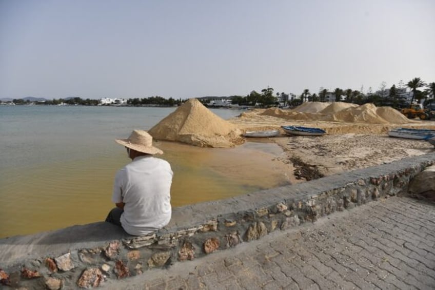 A man looks on as a digger spreads sand on a beach in the tourist town of Hammamet as auth