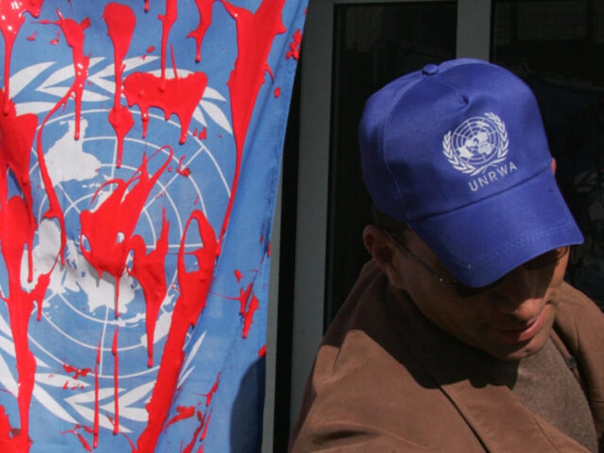 A employee of UN's main agency, UNRWA, stands by a flag covered with red paint during a protest against the Israeli strikes in the Gaza Strip on January 12, 2009 in the West Bank town of Hebron. The UNRWA operating in Gaza suspended operations after a UN-flagged convoy was hit …