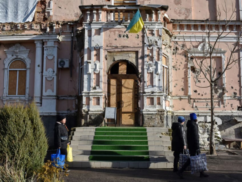 ORIKHIV, UKRAINE - 2024/01/04: Local residents seen walking with their belongings past an old historic building (more than 100 years old) damaged by Russian shelling in Orikhiv. Just a few kilometres from the southeastern front line, Orikhiv has become a ghost town almost two years after Russia launched a full-scale …