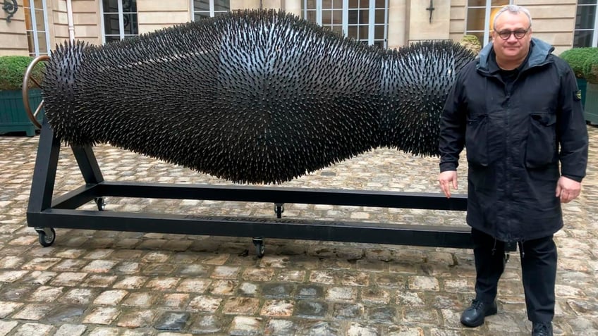 Mikhail Reva next to a sculpture made from war debris