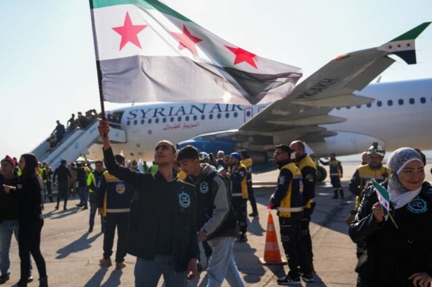 A man lifts an independence-era Syrian flag as passengers disembark in Aleppo, after the f