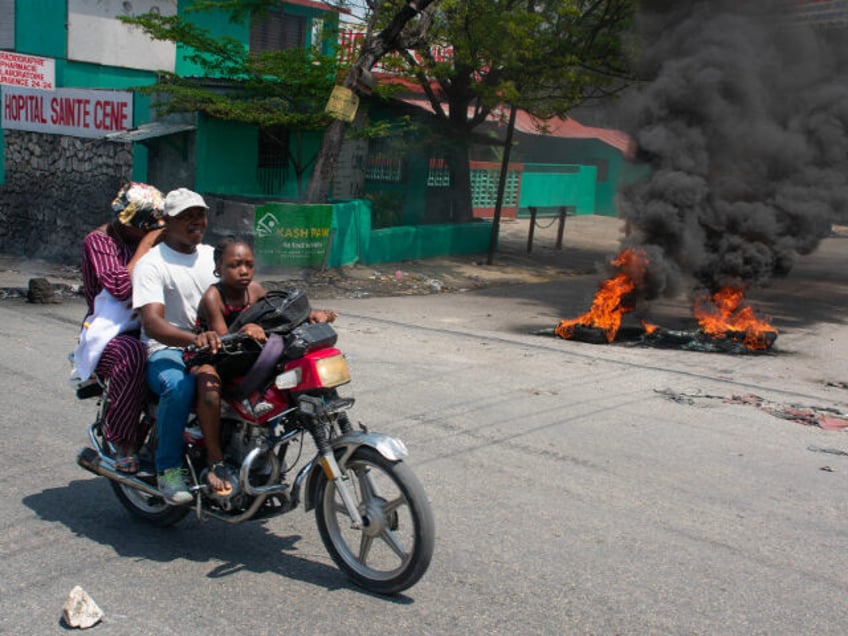 A woman and her child leave the area on a motorcycle after gunshots were heard in Port-au-