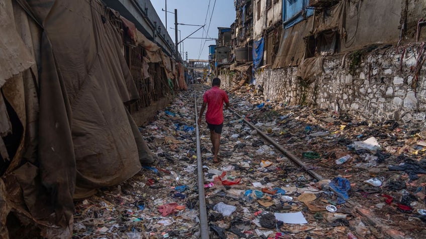 A man walks on a railway track littered with plastic