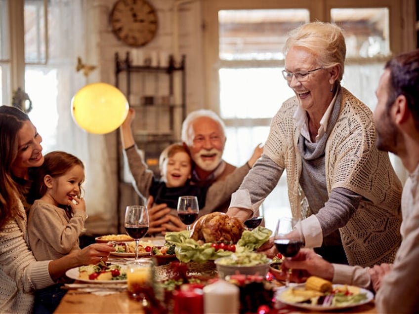 Happy grandmother serving Thanksgiving dinner to her family at dining table.