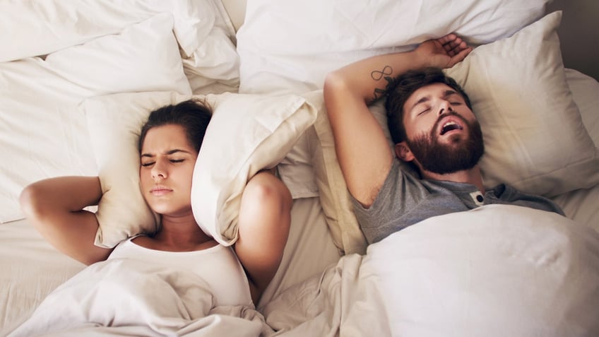 man snores in bed next to woman