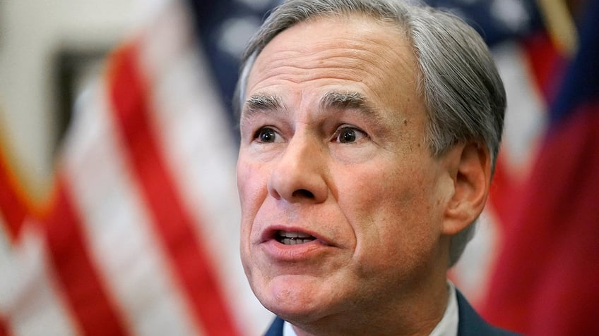 Photo shows close up shot of Greg Abbott while he speaks in front of American flags