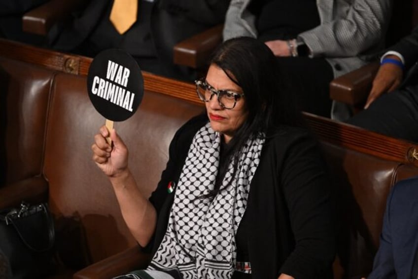 In the cartoon, a woman identified as Rep. Tlaib is seen sitting at a desk next to an expl