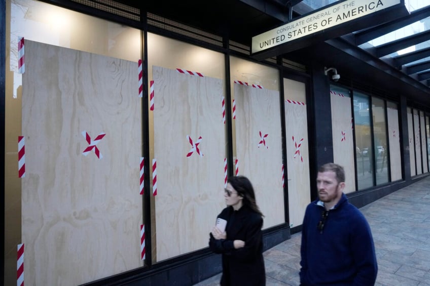 A couple walks past the boarded windows at the U.S. consulate as police investigate the vandalism in Sydney, Monday, June 10, 2024. A suspect is believed to have smashed nine holes in the reinforced glass windows of the building in North Sydney after 3 a.m., a police statement said. (AP Photo/Rick Rycroft)