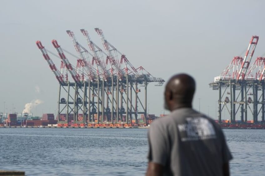 A man walks along a pier in Bayonne as cranes are visible at Port Newark in New Jersey, on