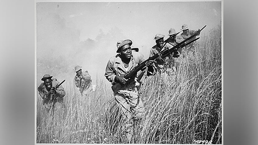 Soldiers in the all-African American 92nd Infantry Division carry their firearms through a field.