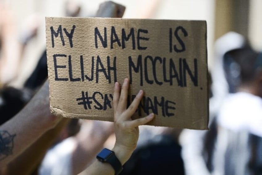 A woman holds up a sign as people rally outside the Aurora Police Department Headquarters